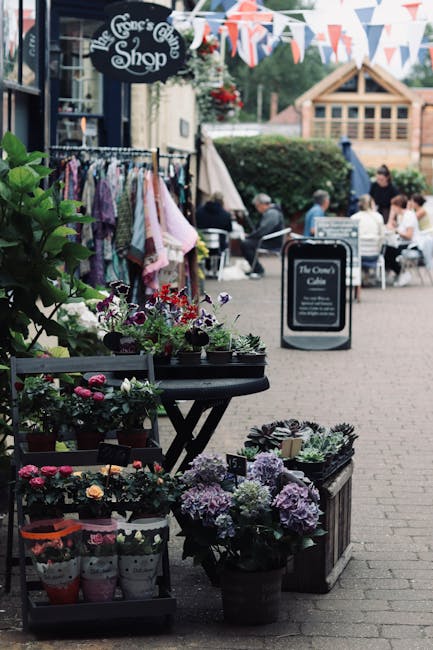 An outdoor flower display outside The George’s Gift Shop on St Pauls Cray High Street, featuring potted flowering plants and fresh floral arrangements in various shades of purple, pink, and white. T